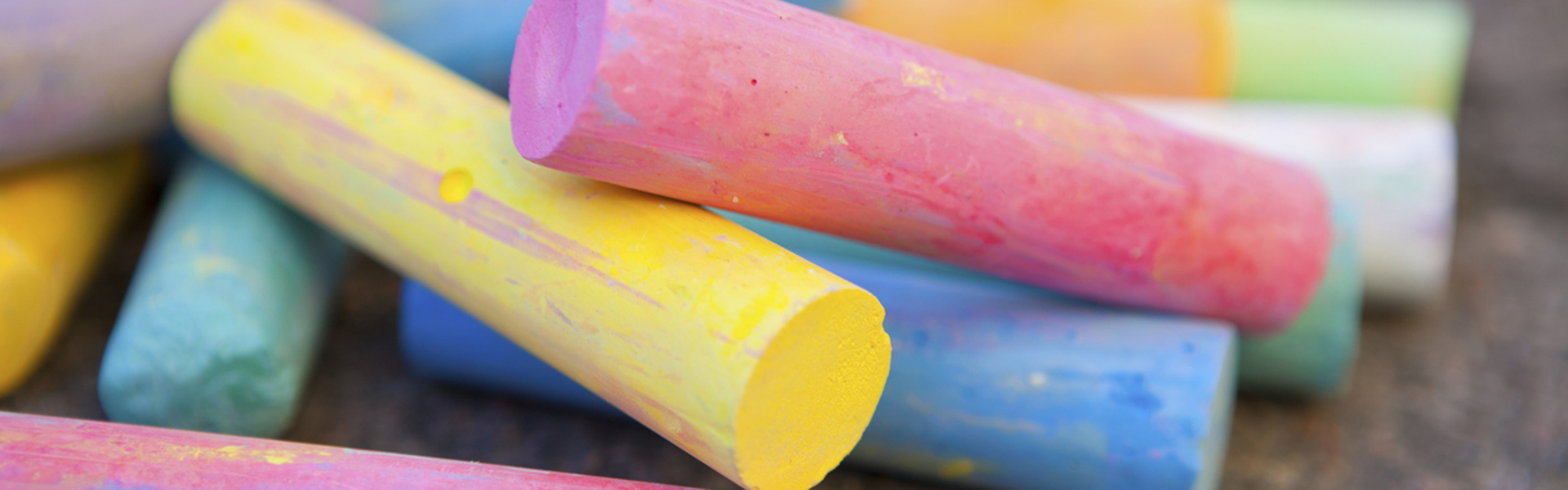 pink yellow and blue coloured chalk sticks on a tarmac floor