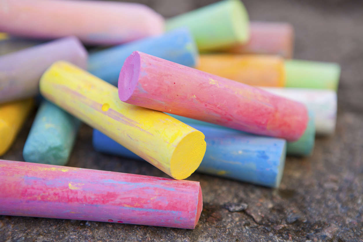 pink yellow and blue coloured chalk sticks on a tarmac floor