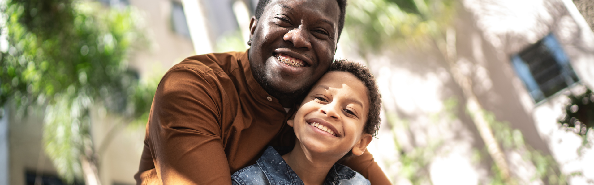 Main image: a father and son hugging and smiling outside in the sun.