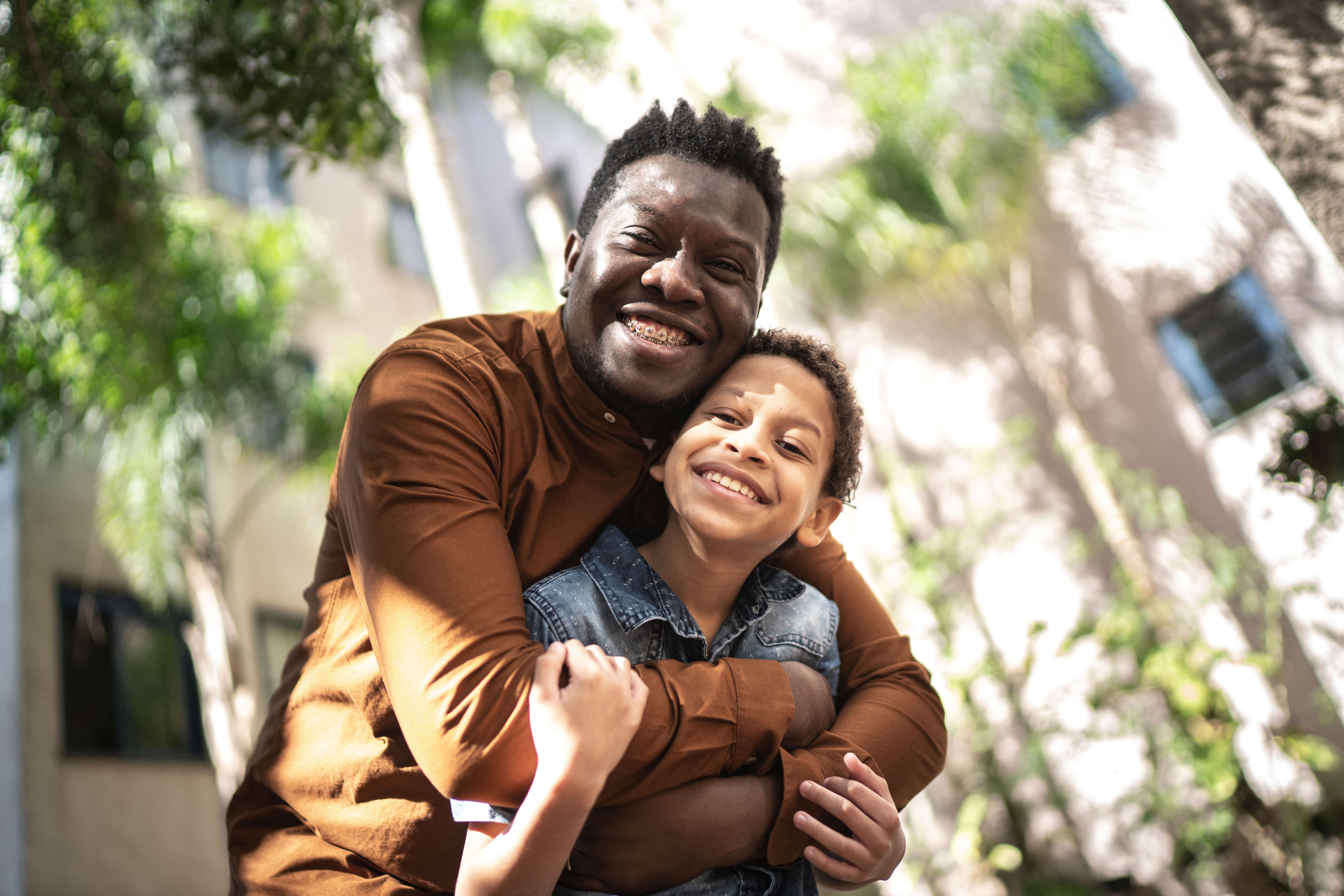 Main image: a father and son hugging and smiling outside in the sun.