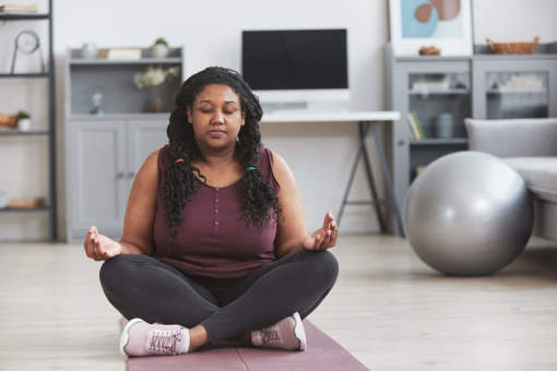 a woman sat cross legged on the living room floor and meditating