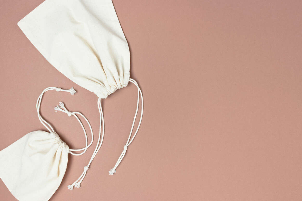 two cream canvas drawstring bags on a brown background
