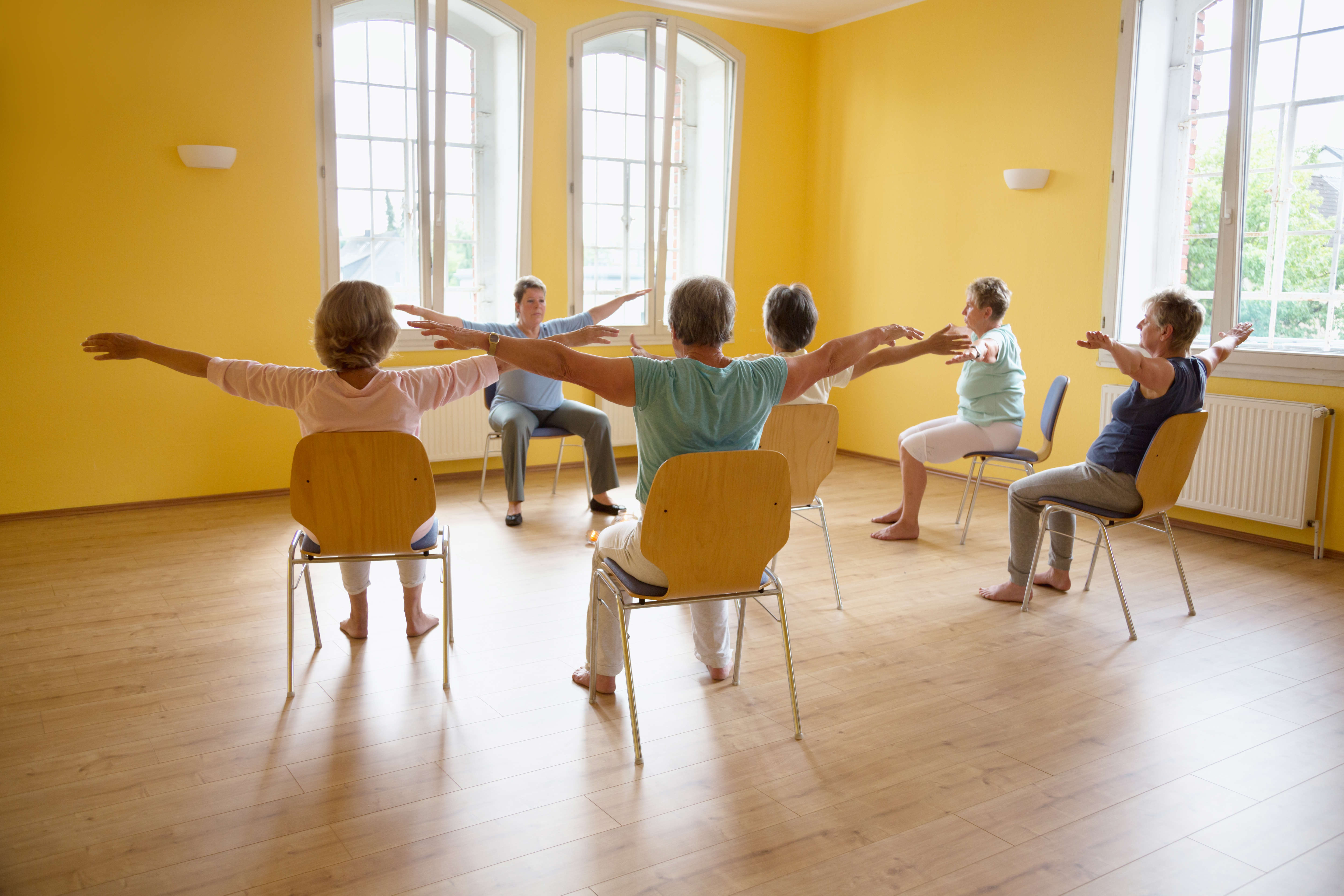 Main image: a group of people taking part in a seated Parkinson's dance class, in a bright yellow room.