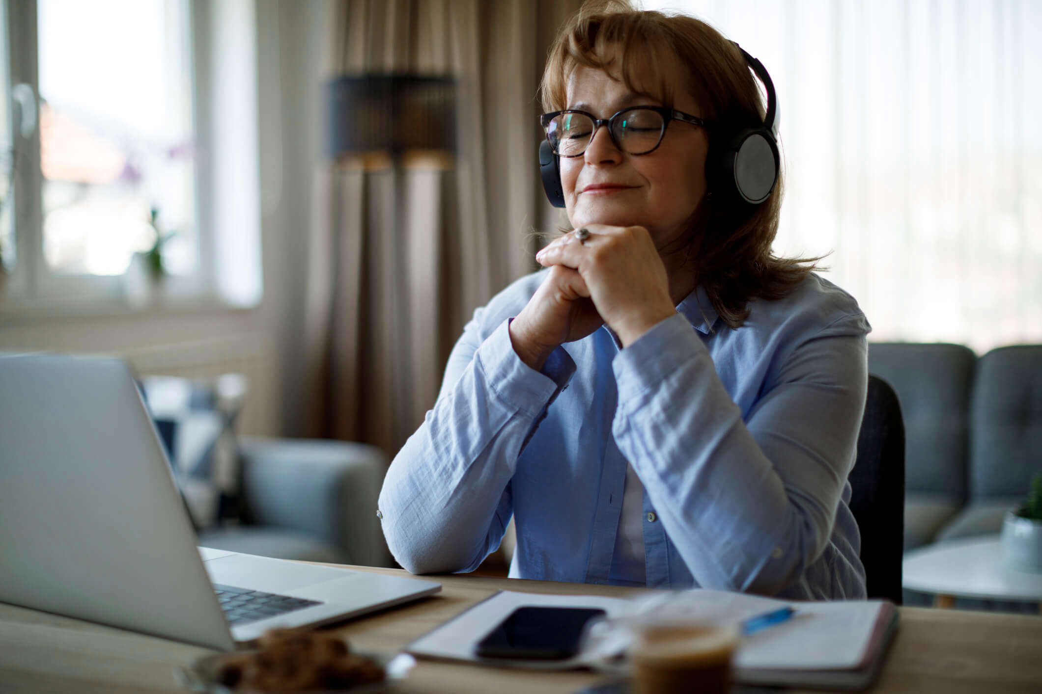 a woman sat a desk with her eyes closed wearing headphones and meditating