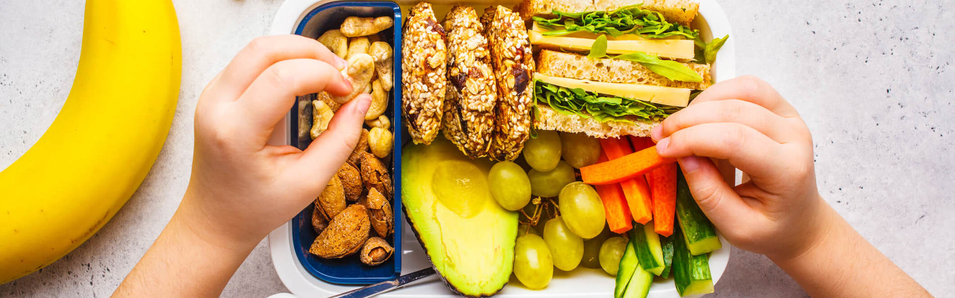 A lunch box filled with nuts and avocado and graps and carrot and cucumber and sandwiches