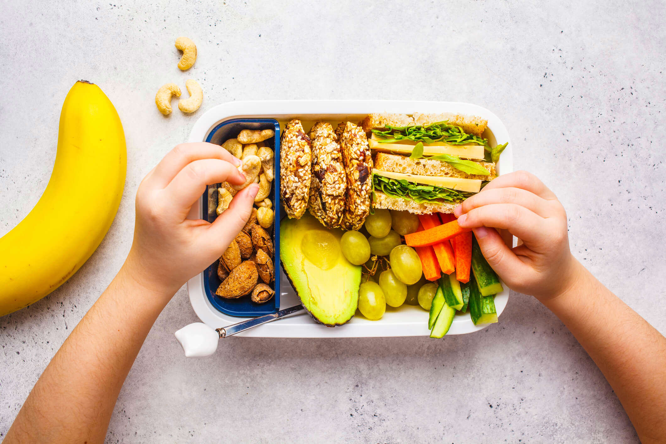 A lunch box filled with nuts and avocado and graps and carrot and cucumber and sandwiches