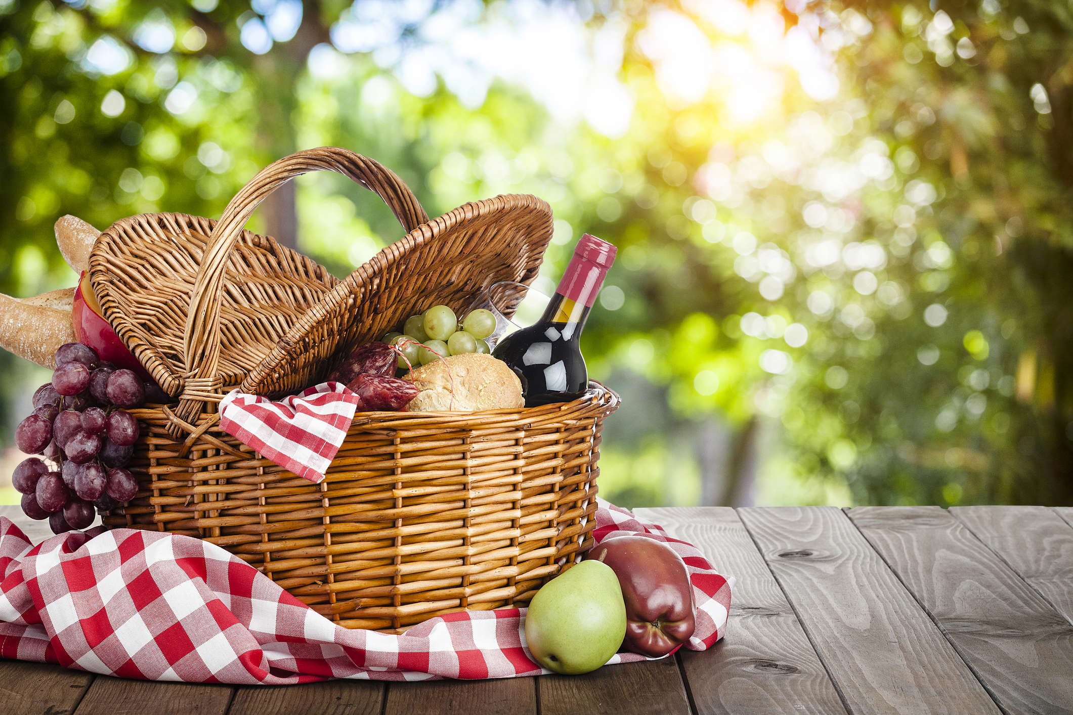 a picnic basket on a red and white check gingham pattern picnic blanket filled with wine and cheese and grapes