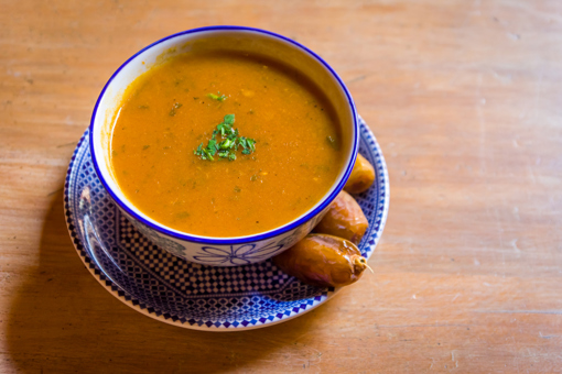 Main image: A bowl of Moroccan bissara, vegan fava bean soup. On a wooden table with herbs on top 