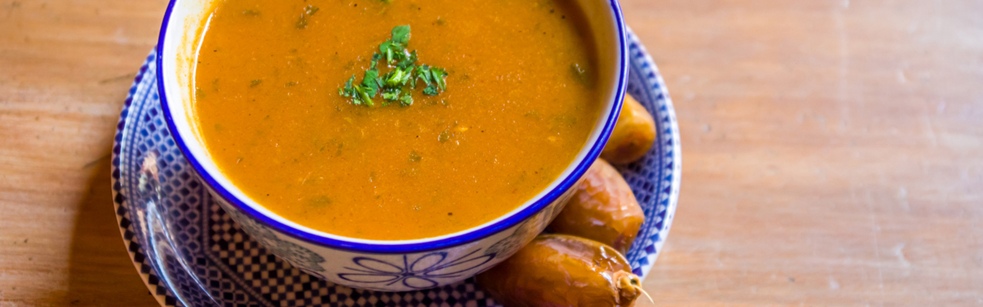 A steaming bowl of soup on a wooden table with herbs on top 