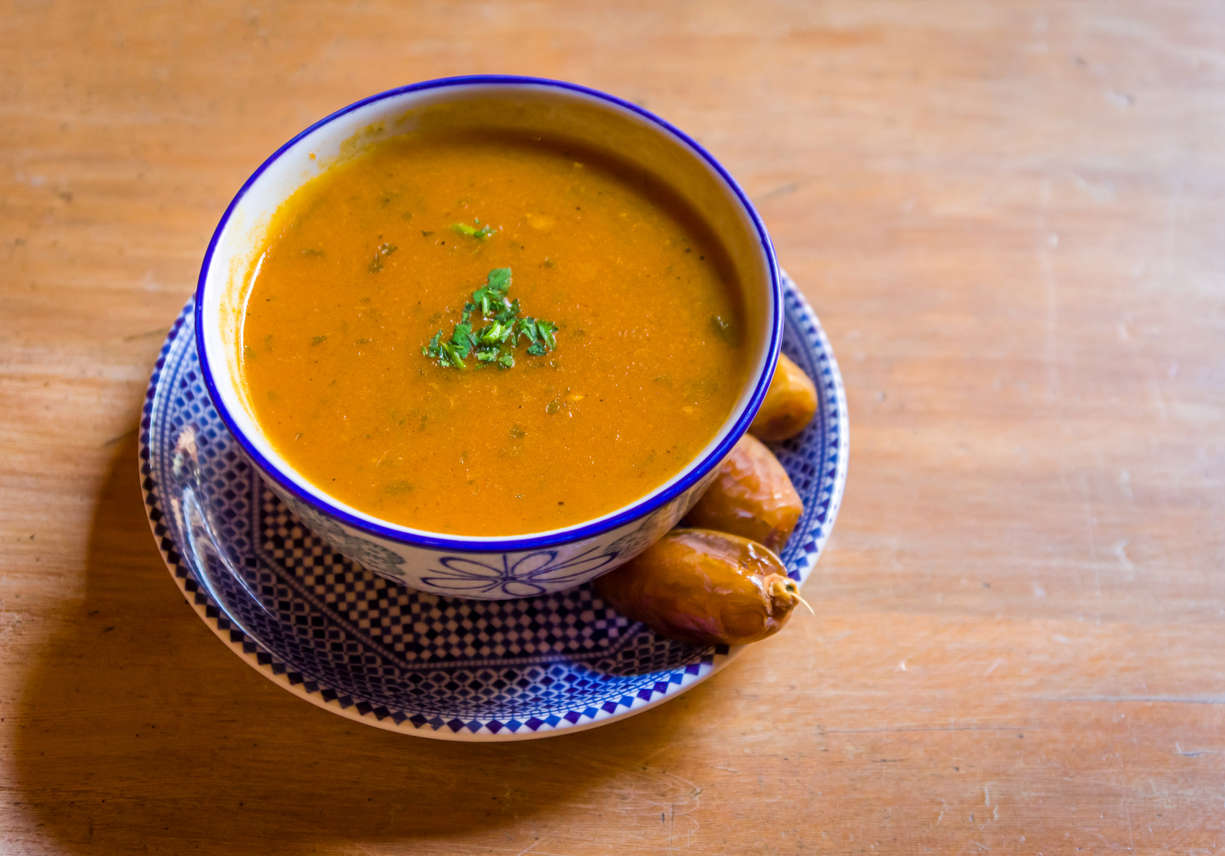 A steaming bowl of soup on a wooden table with herbs on top 