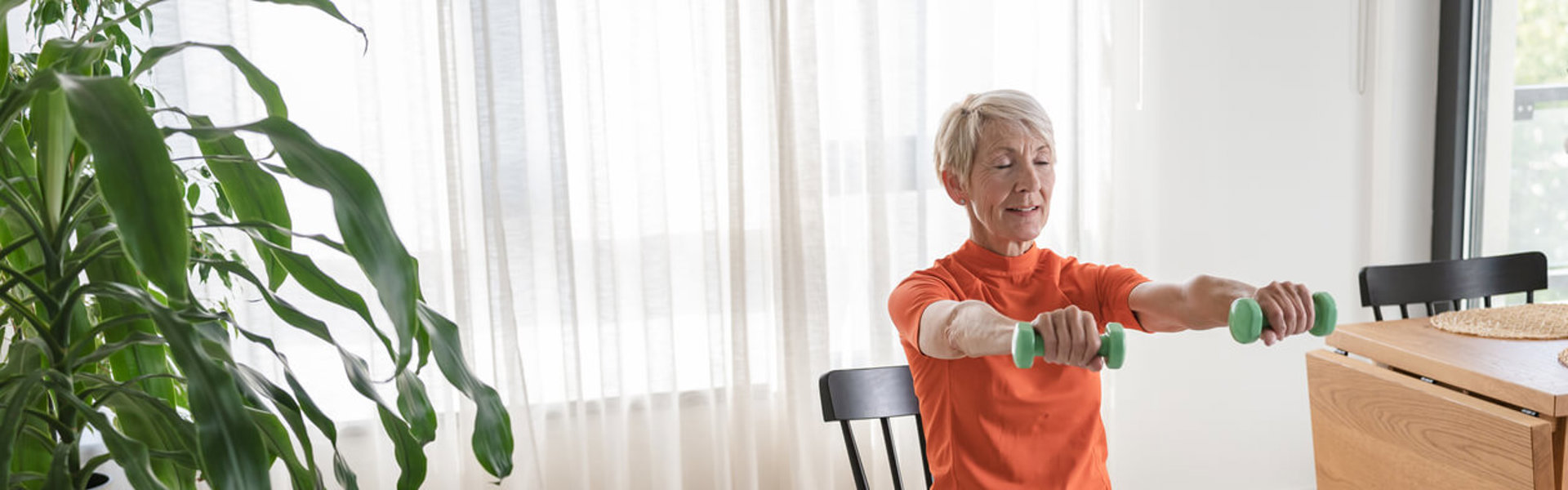 Smiling beautiful senior woman health instructor doing chair exercises with dumbbells