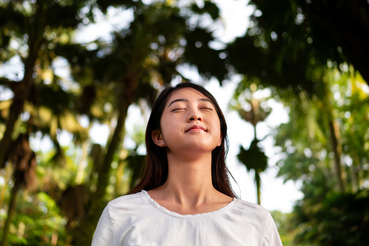 a woman stood in nature with eyes closed looking calm