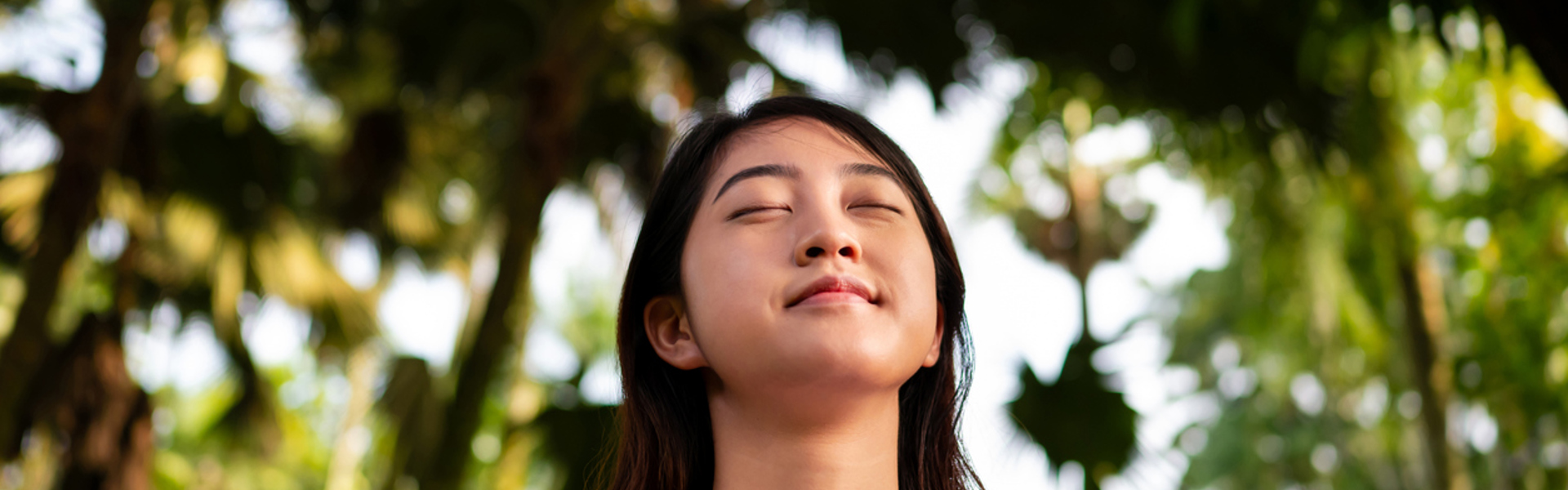 a woman stood in nature with eyes closed looking calm