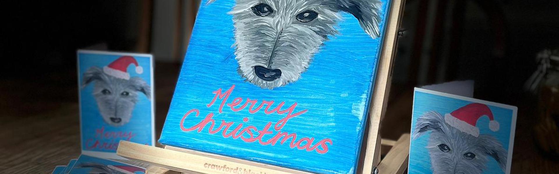 an easel with a portrait of a pet dog wearing a Christmas hat on a blue back ground