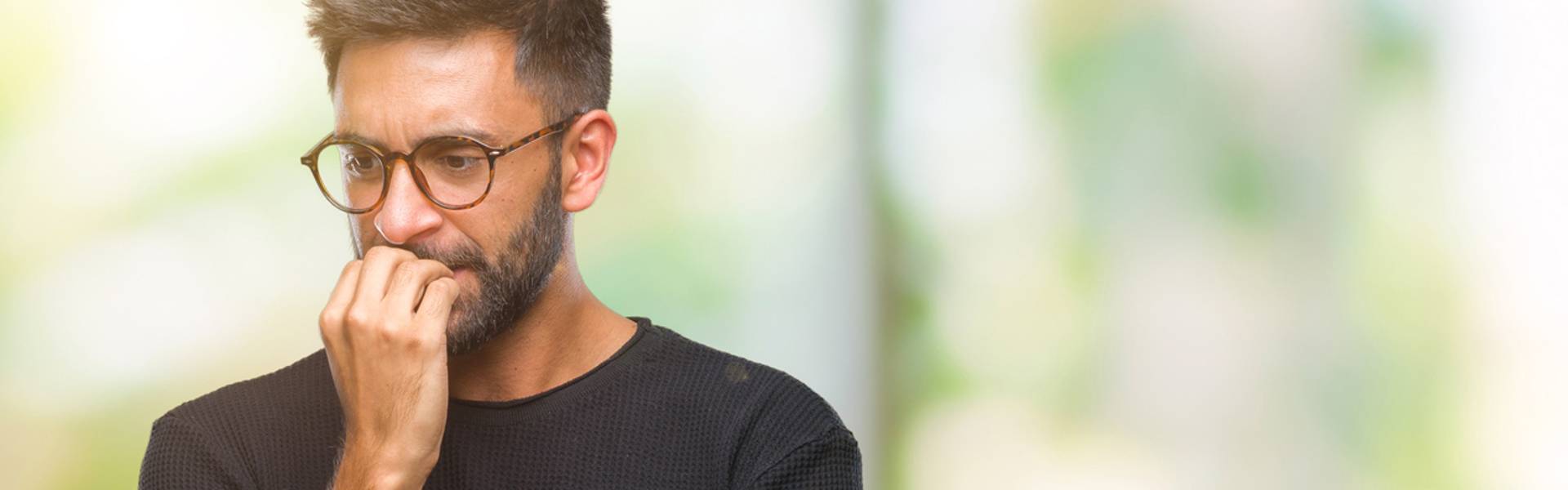 a man wearing glasses and biting his nails looking anxious