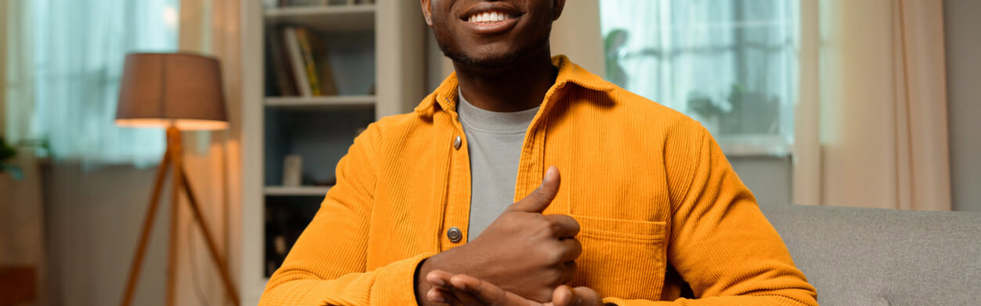 a man in a orange corduroy jacket using sign language in his living room 