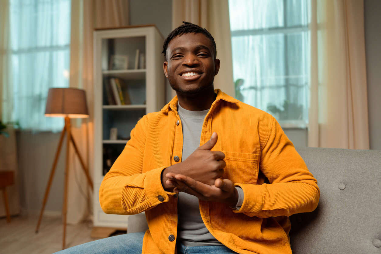 a man in a orange corduroy jacket using sign language in his living room 