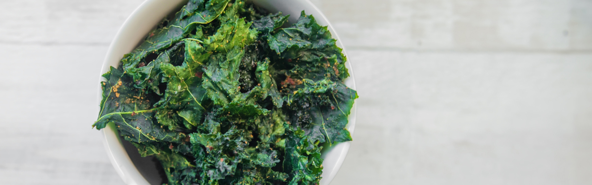 A bowl of crispy kale salad garnished with Moroccan seasoning on a white table.