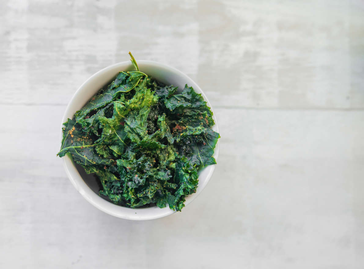 A bowl of crispy kale salad garnished with Moroccan seasoning on a white table.