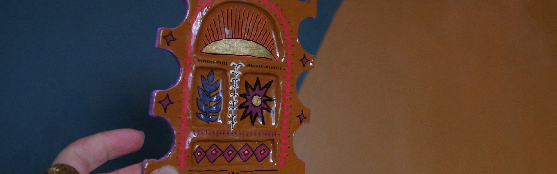 Main image: an air dry clay trinket dish, painted brown, with red, blue and purple funky patterns.