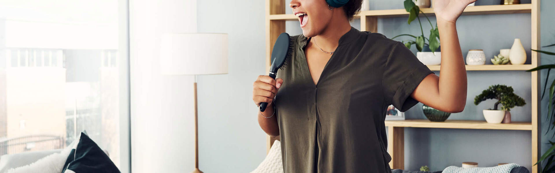 a woman singing into a hairbrush in the living room wearing headphones