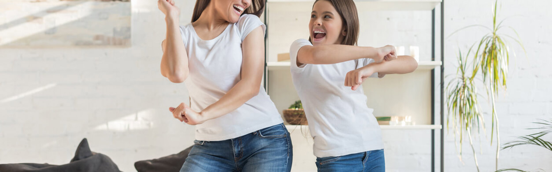 A woman and a girl wearing white t-shirts and blue jeans dancing in the living room