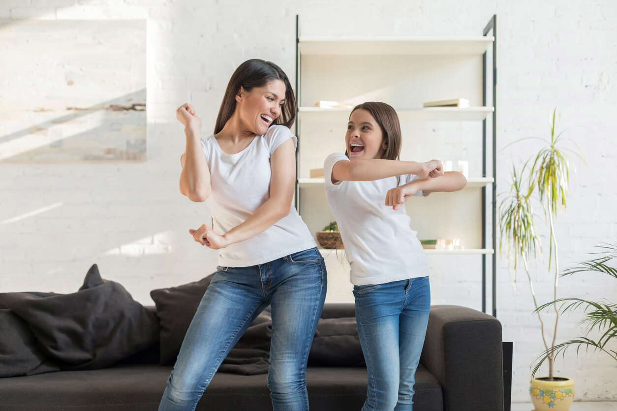 A woman and a girl wearing white t-shirts and blue jeans dancing in the living room