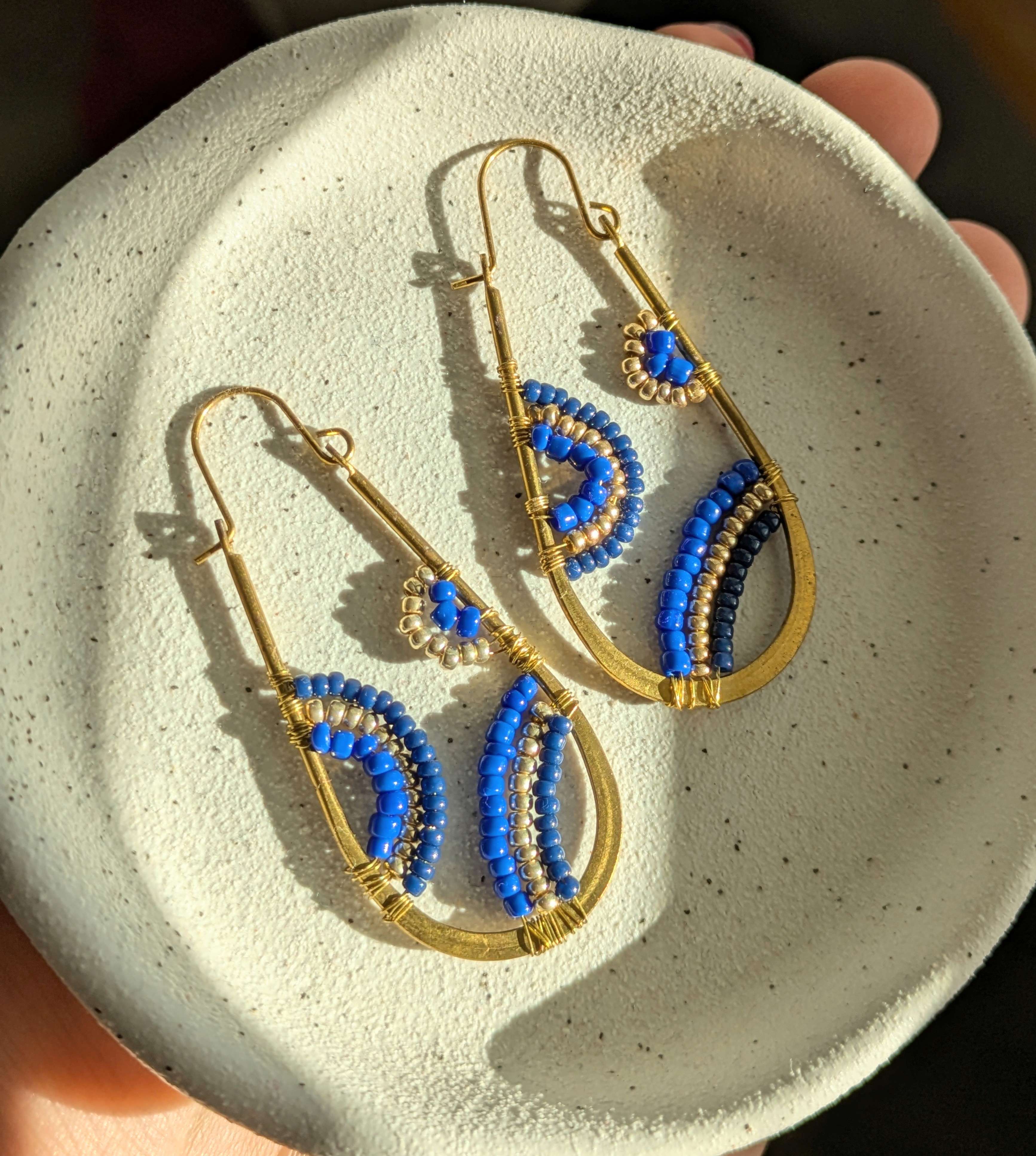 Photo of handmade beaded earrings, with gold metal and blue beads in arch shaped patterns in the hoops.