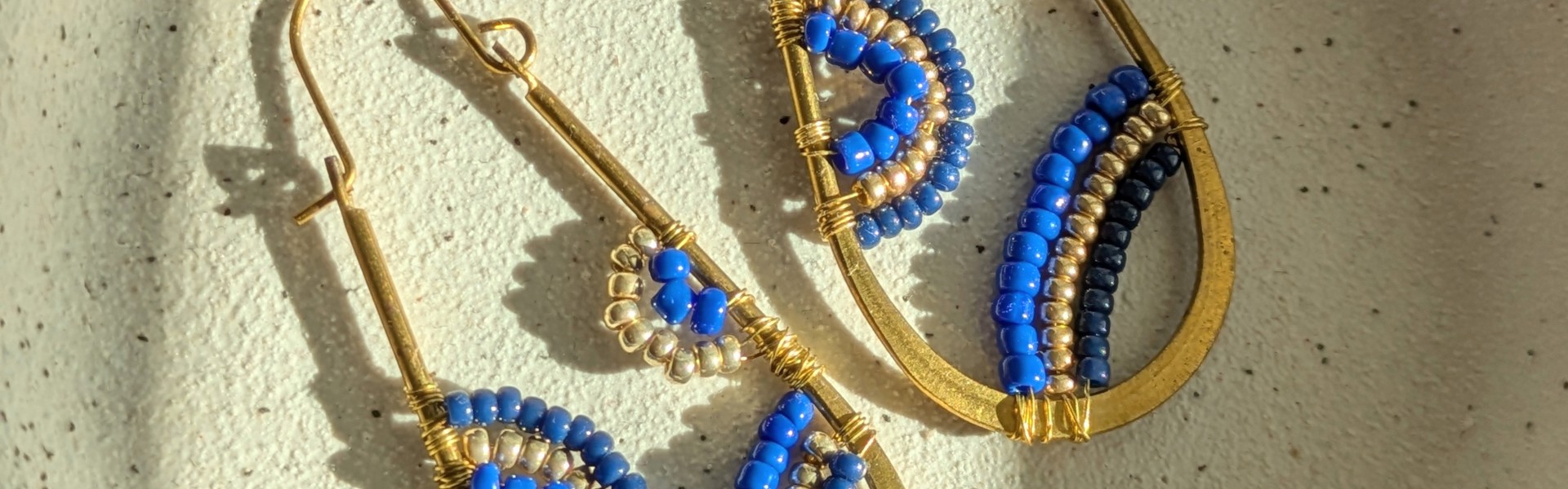Photo of handmade beaded earrings, with gold metal and blue beads in arch shaped patterns in the hoops.