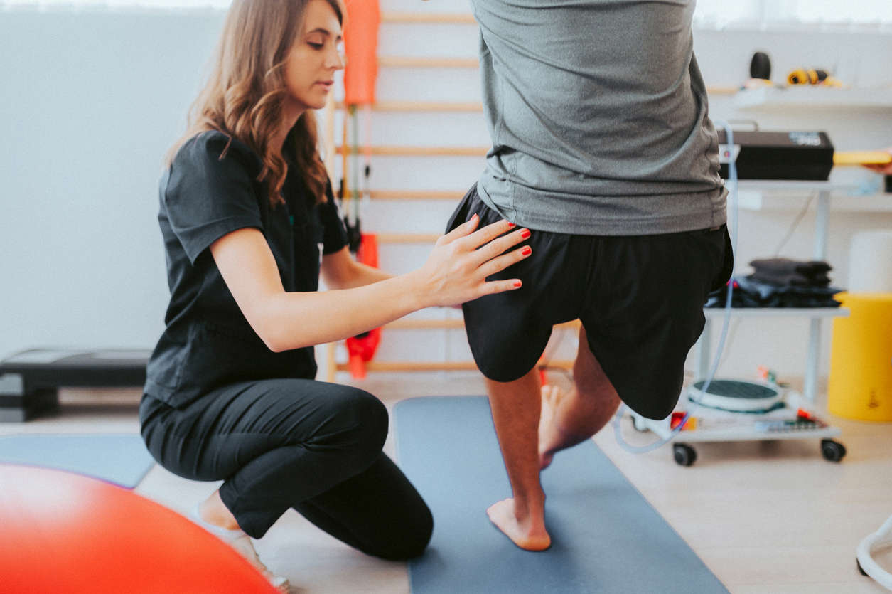 a female trainer assisting a man into a pistol squat position