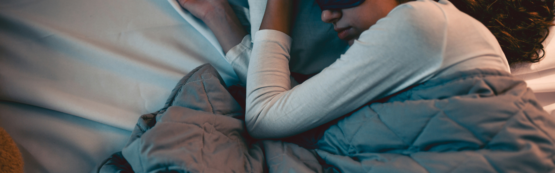 A woman sleeping in bed with a back sleep mask on after a gentle EFT tapping for restful sleep session.