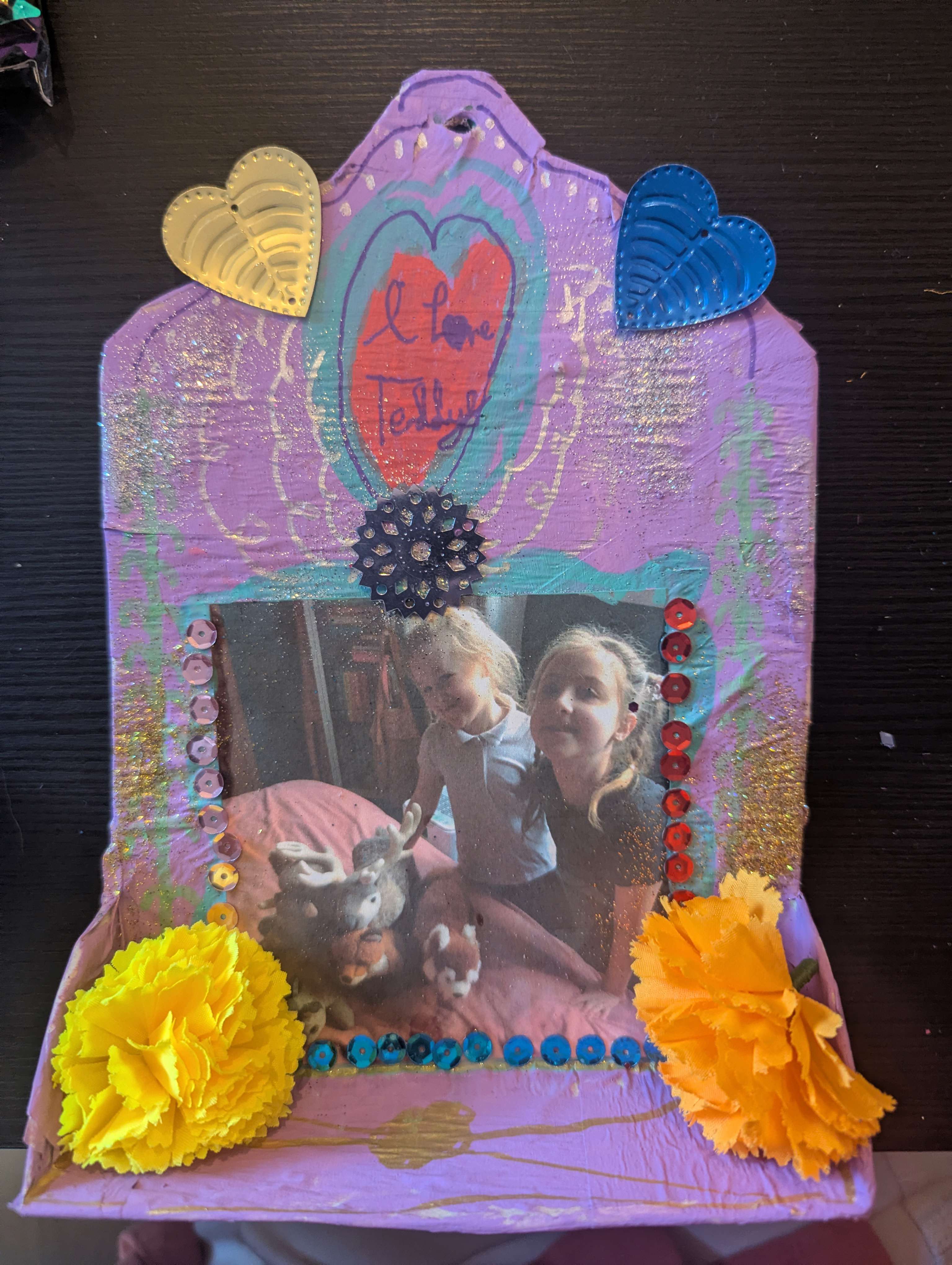 Main image: a mini altar, or DIY cardboard shrine painted in purple, with a photo in the middle and decorations. 