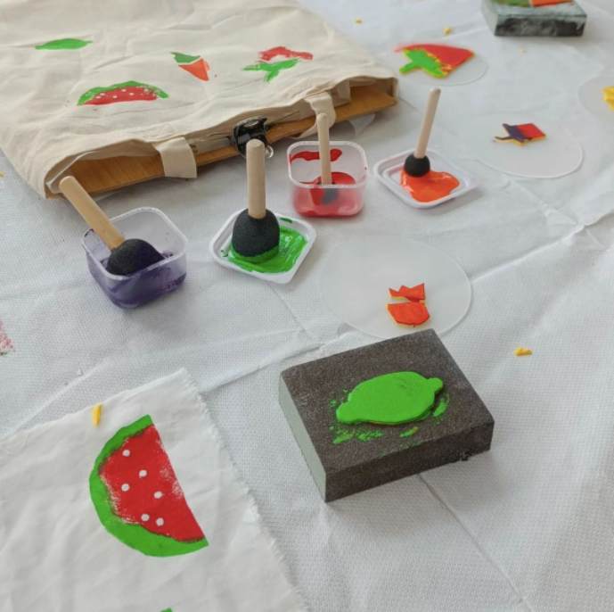 Homemade stamp making tools on a white table cloth in various primary colour paints