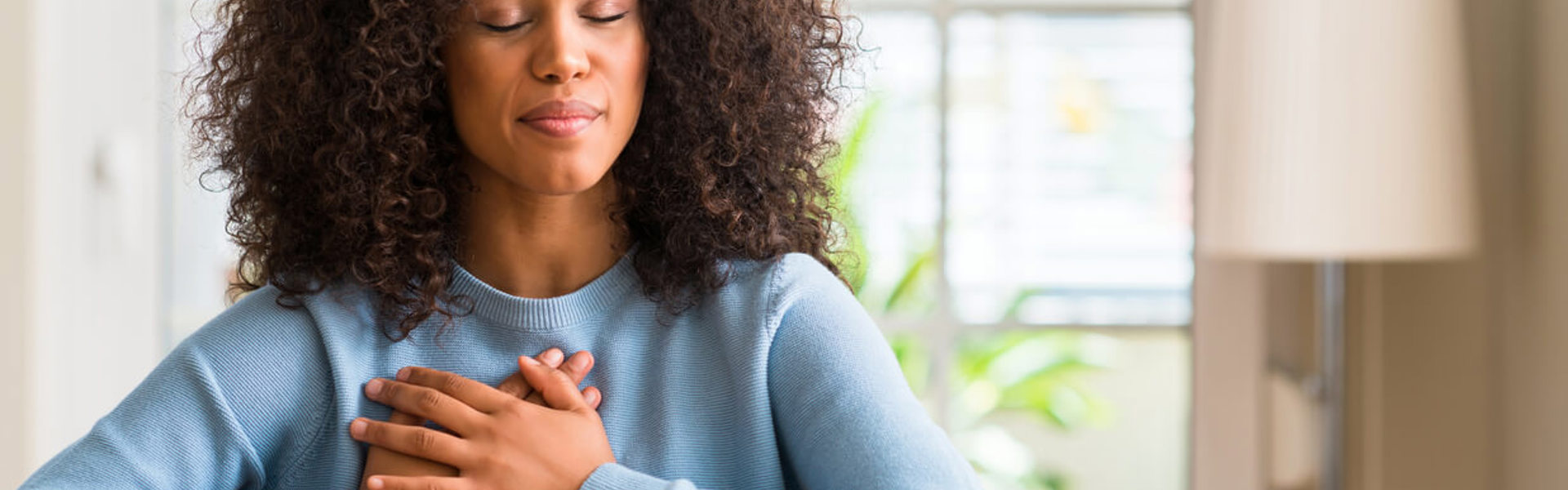 a woman wearing a blue knit jumper sat with her hands to her chest and eyes closed