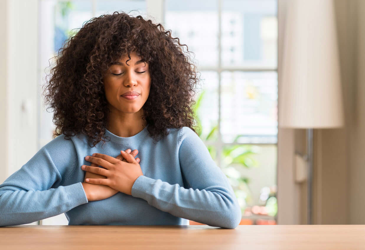 a woman wearing a blue knit jumper sat with her hands to her chest and eyes closed