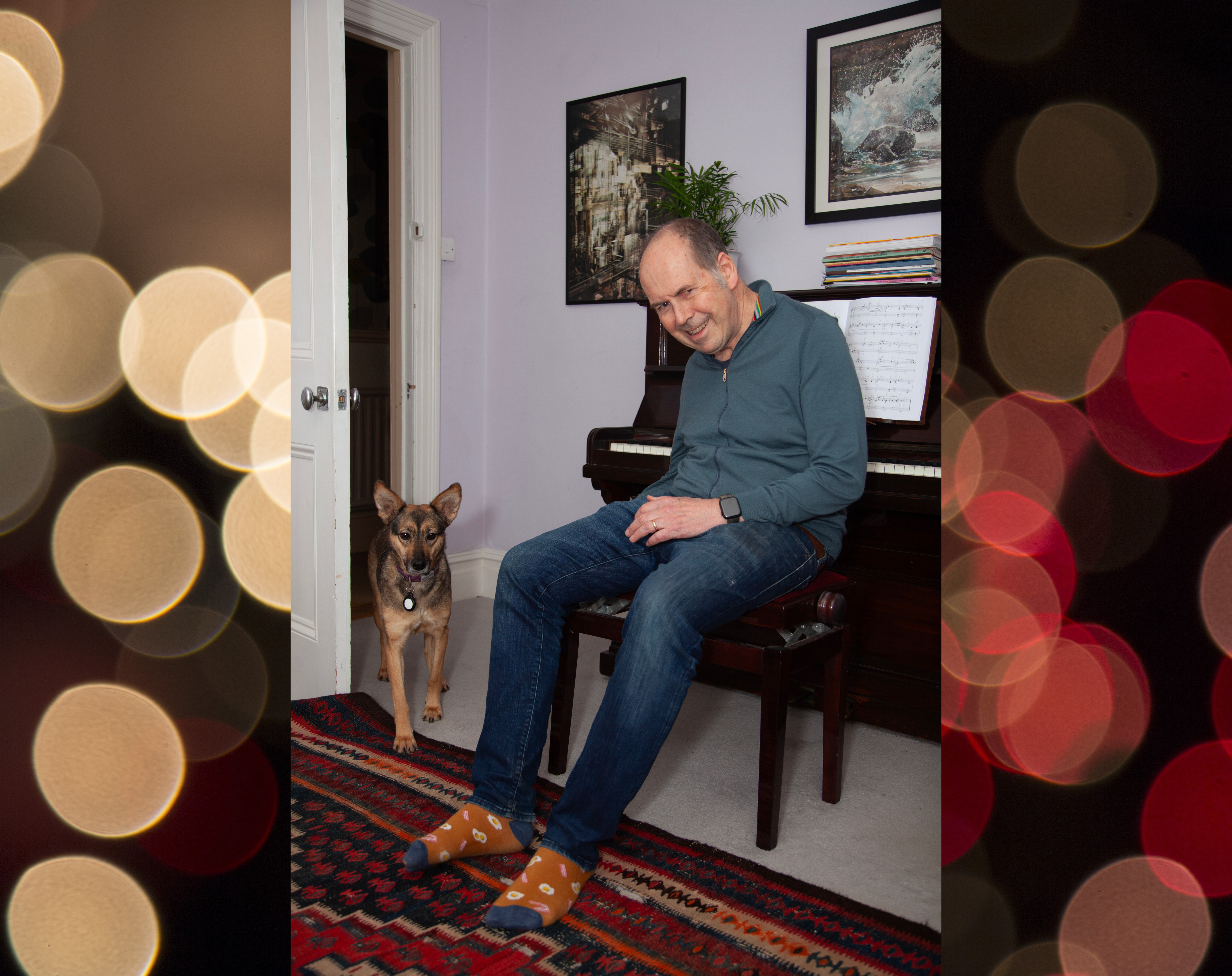 A photo of Rory Cellan-Jones and his rescue dog Sophie, from Romania. Rory is sat in front of a piano, with Sophie walking into the room. With a background image of gold and red orbs on a black background.
