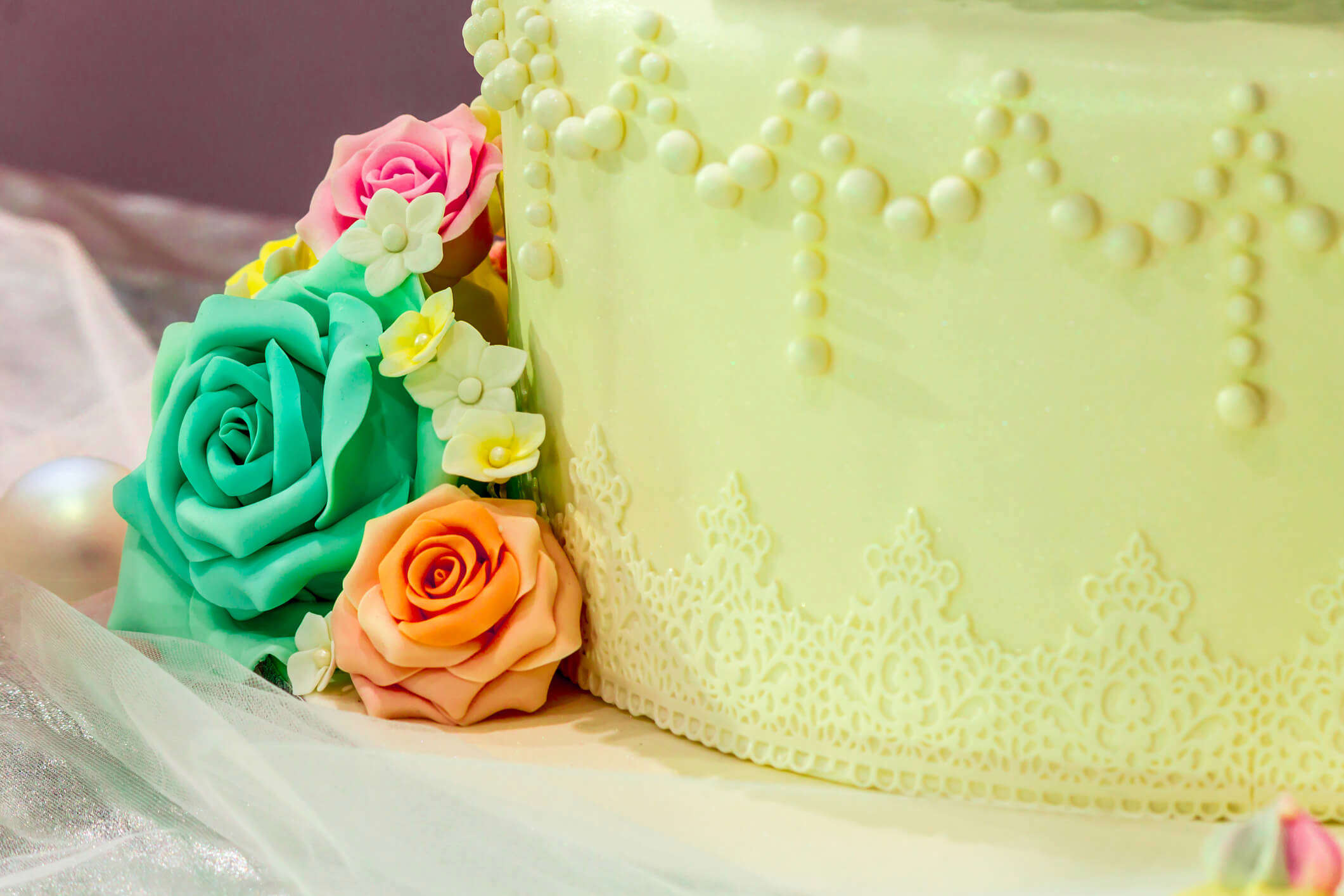 a close up of a cake covered with green sugar paste and decorated with green orange and yellow sugar paste roses