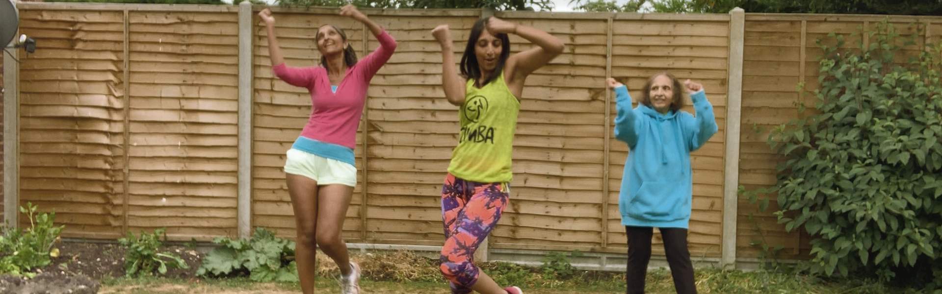 Main image: three women of different ages dressed in colourful clothing dancing during a Zumba class.