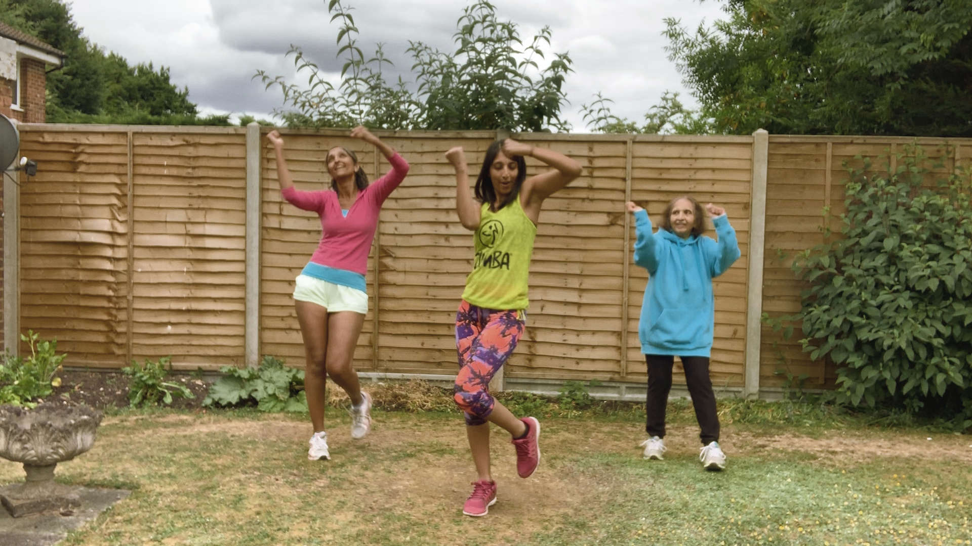 Main image: three women of different ages dressed in colourful clothing dancing during a Zumba class.
