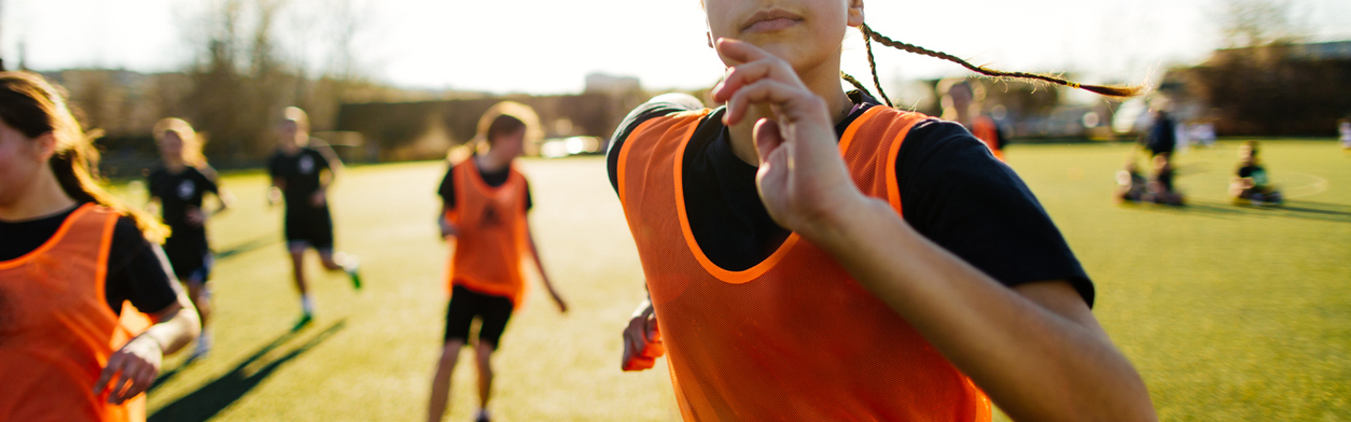a woman in an orange sports bib running on a football field