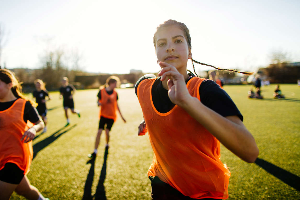 a woman in an orange sports bib running on a football field