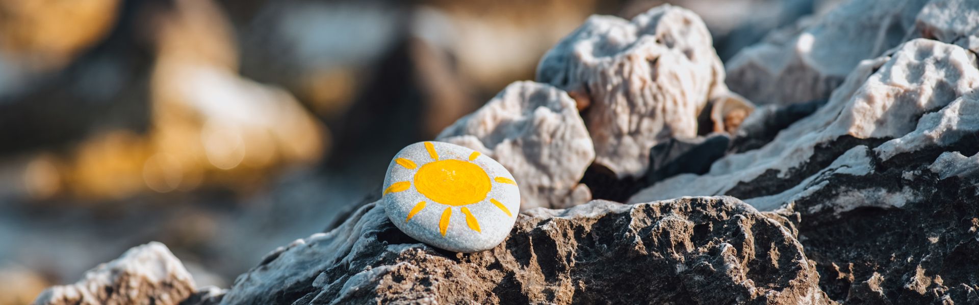 a painted pebble resting on a rockpool at the beach with a yellow sun painted on it 