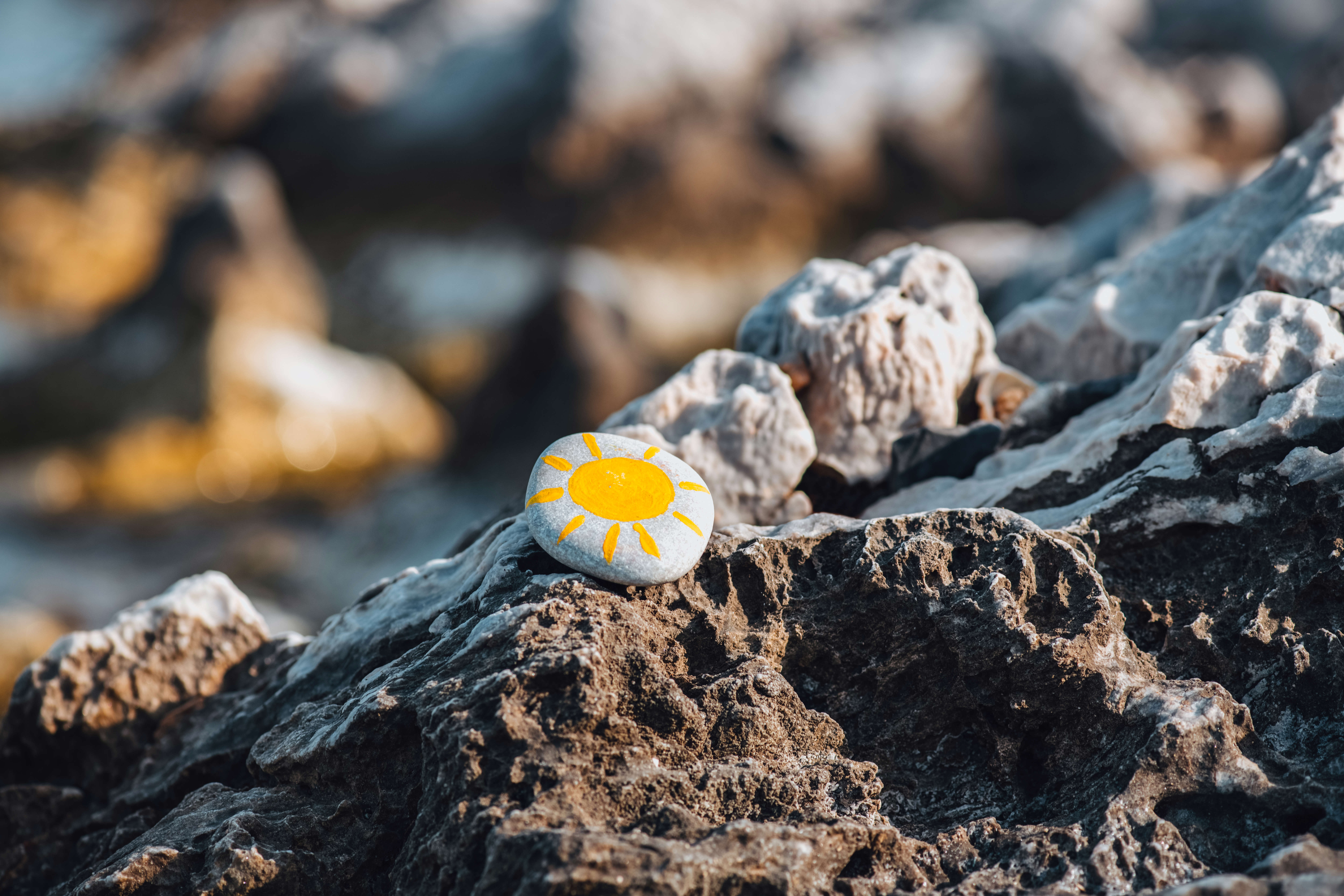 a painted pebble resting on a rockpool at the beach with a yellow sun painted on it