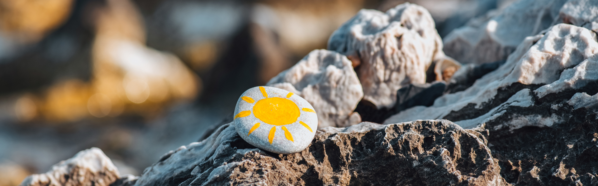 a painted pebble resting on a rockpool at the beach with a yellow sun painted on it