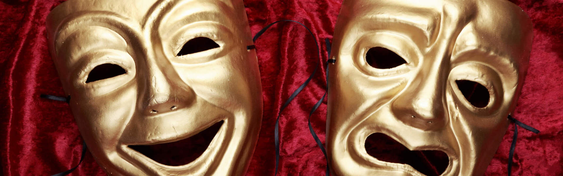 two gold theatre masks on a red velvet background
