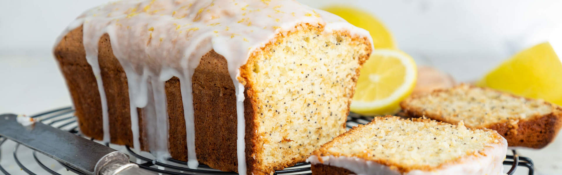 a lemon and poppy seed drizzle cake on a cooling rack surrounded by lemons