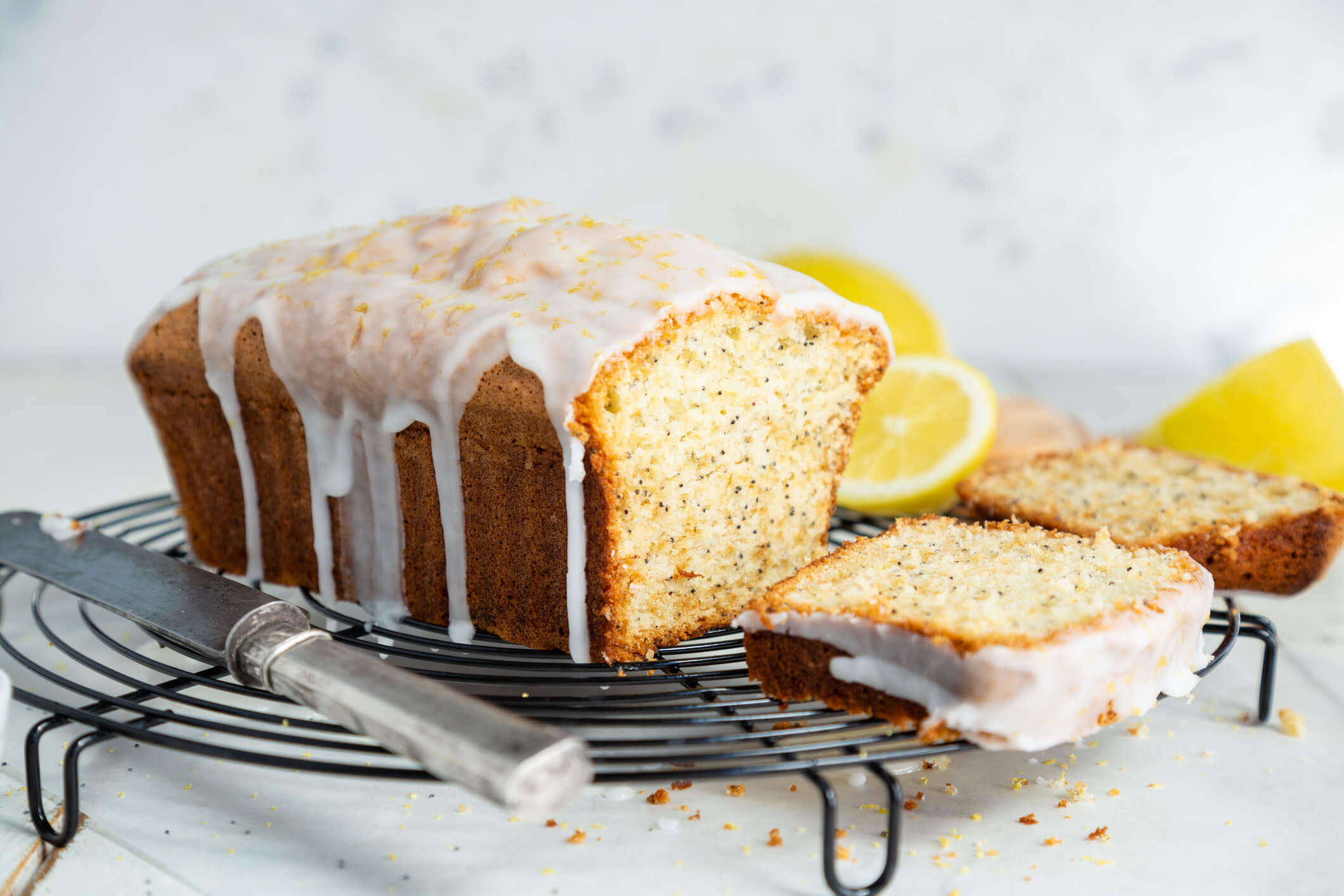 a lemon and poppy seed drizzle cake on a cooling rack surrounded by lemons