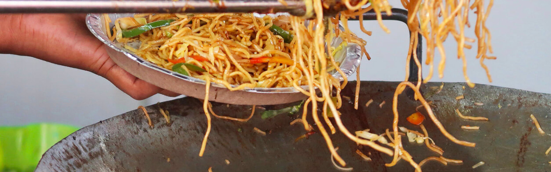 A person serving spiced chicken chow mein into a foil plate