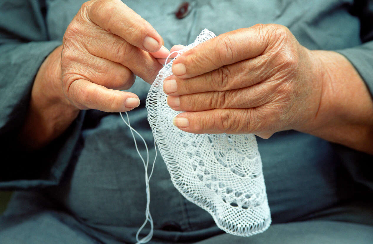 a close up of someone using a needle and thread to sew a white doily decoration