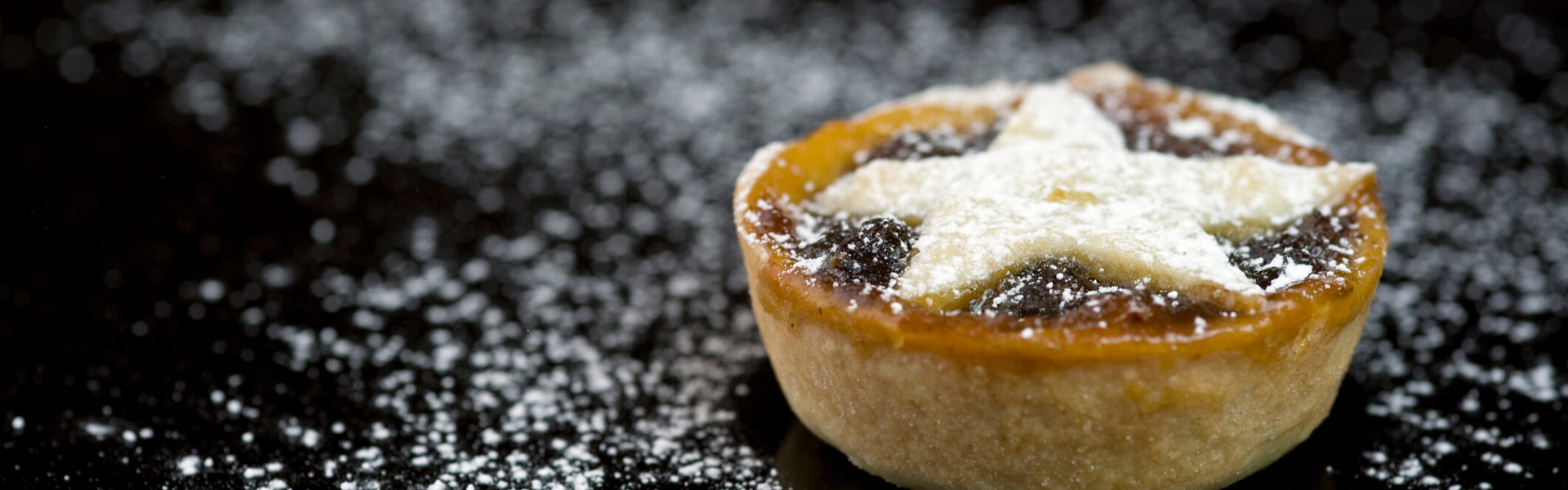 a close up of a mini mince pie with a star shaped top dusted with icing sugar